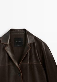 Braune Lederjacke mit einem Reverskragen, Ein-Knopf-Verschluss und kontrastierenden Nähten. Innen befindet sich ein schwarzes Etikett mit dem Markennamen.