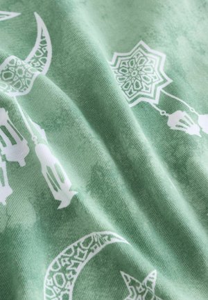 Green fabric featuring white patterns of crescent moons and geometric lanterns, displaying a soft texture with a subtle gradient.