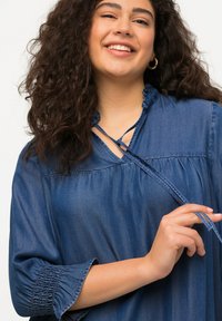 Denim-paita rentoa istuvuutta, rypytetty kaula-aukko ja 3/4-hihat. Sisältää nauhasolmuja kaulassa ja kerättyjä hiha-aukkoja. Sininen väri.