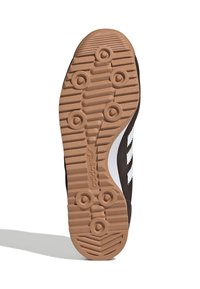 Sole di scarpa sportiva nera con superficie in gomma strutturata, dotata di tacchetti circolari e un design a strisce bianche. Accentuata da un tallone marrone.