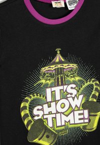 Schwarzes T-Shirt mit lila Kragen, das ein buntes Grafikdesign eines Karussells, gestreifte Akzente und fettgedruckten Text mit der Aufschrift "JETZT GEHT'S LOS!" zeigt.