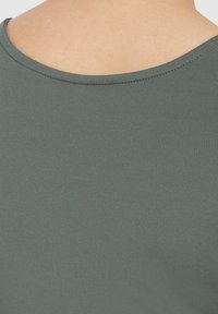 Tmavě zelený, elastický top z hladké tkaniny s kulatým výstřihem, na kterém je zobrazen pouze zadní část oděvu.