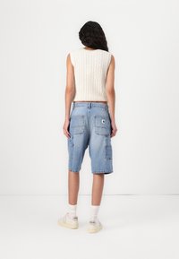 Ljusblå denim cargo shorts med flera fickor, kombinerat med en krämfärgad ribbad ärmlös topp. Vita sneakers fulländar stilen.