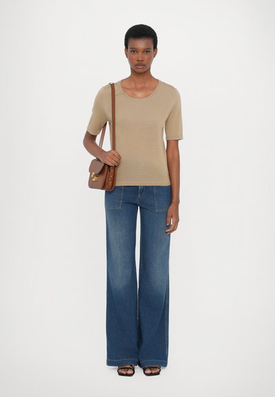 Beige strikket topp med korte ermer kombinert med vide blå jeans. Brun skulderveske og svarte åpen tå-sko fullfører antrekket.