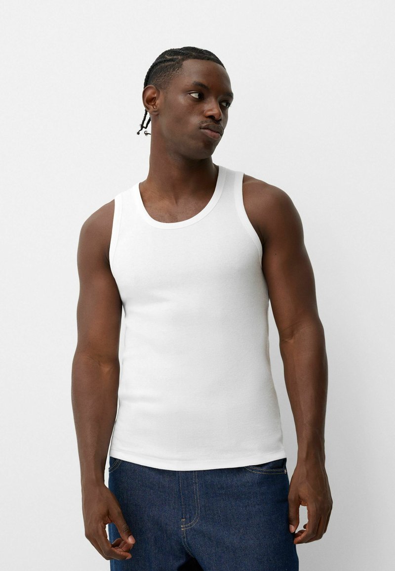 Vit bomullstanktop med rund halsringning, åtsittande form och breda axelremmar, bärs med mörkblå denimjeans.