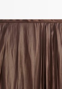 Hnědá saténová sukně s vertikálními záhyby a hladkou texturou. Má jednoduchý pas a elegantně splývá, vytvářejíc plynulý vzhled.
