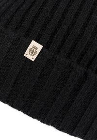 Close-up of ribbed black knit fabric with a small beige tag featuring a detailed emblem with a crown and shield.