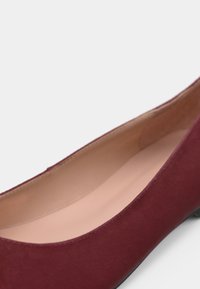 Shoe plana bordô feita de camurça macia com bico arredondado e forro interno suave. Apresenta um design minimalista com um salto de perfil baixo.