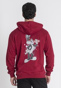 Felpa rossa con cappuccio, caratterizzata da una grande grafica stampata di un personaggio dei cartoni animati sulla schiena, con dettagli in bianco e nero e schizzi blu.