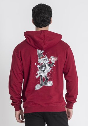 Rød hættetrøje med et stort trykt grafisk motiv af en tegneseriefigur på ryggen, med sort-hvide detaljer og blå sprøjt.