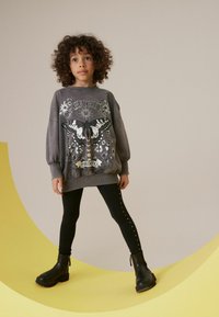 Grå överdimensionerad sweatshirt med fjärilstryck och text; matchad med svarta leggings prydda med nitar; avslutad med svarta ankelskor.