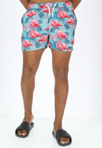 Swim trunks with a turquoise background featuring pink flamingo and green leaf patterns. Elastic waistband with white drawstring.