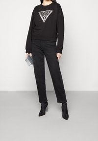 Sudadera negra recortada con un diseño metálico triangular, combinada con jeans negros de pierna recta y botines negros puntiagudos.