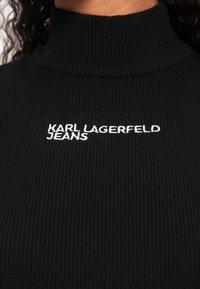 Μαύρο πλεκτό πουλόβερ με ριγέ λαιμόκοψη και λευκό κεντημένο λογότυπο "KARL LAGERFELD JEANS" στο στήθος.