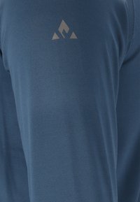 Camicia a maniche lunghe blu realizzata in tessuto liscio con un piccolo logo grigio sulla parte superiore del braccio. Il design è ergonomico e presenta linee pulite.