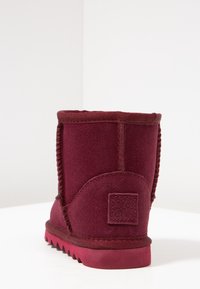 Botín de ante burdeos hasta el tobillo con una superficie texturizada, costuras reforzadas y una suela de goma con un patrón de zigzag. Tacón plano y parche con logo.