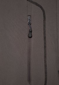 Gros plan d'un tissu gris foncé avec une fermeture éclair verticale et une petite tirette noire avec un motif empreinte de patte.