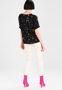 Top negro de manga corta con un patrón floral multicolor, combinado con jeans color crema y botas de tacón de aguja rosa brillante.