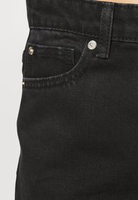 Mustat farkut, joissa on sileä pinta, viisi taskua ja hopeiset yksityiskohdat, kuten nappi ja niitit.