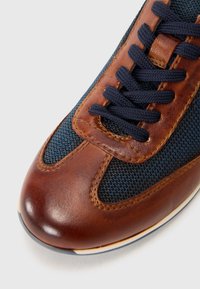 Pruun nahast ja tumesinine silmesh sneaker, millel on tumesinised paelad, ümar varvas ja kontrastsete õmblustega õmblustel. Lamedat kummitalda on näha.