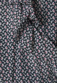 Tissu noir avec de petites fleurs blanches, chacune avec un centre rouge, présentant un détail de nœud torsadé.