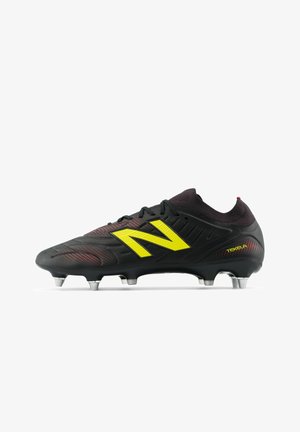 Chaussure de football noire avec des accents rouges, dessus texturé, grand logo jaune et crampons argentés sur une semelle noire pour la traction.