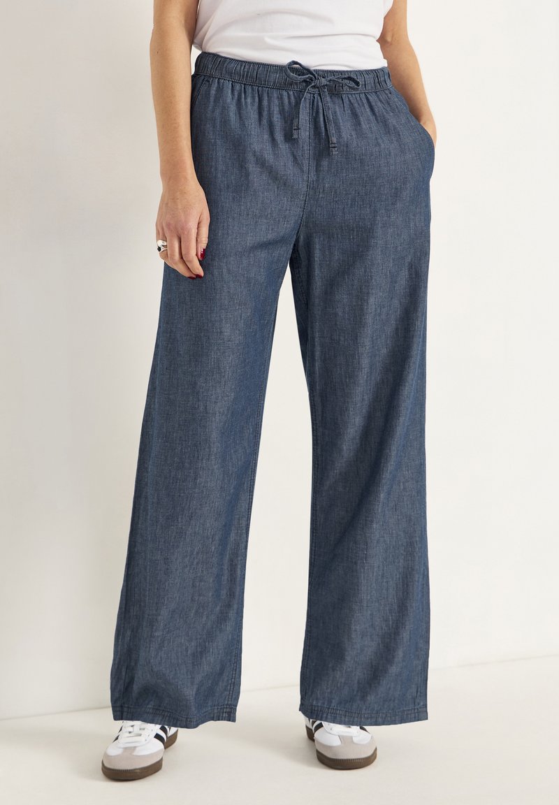 Breda jeans med elastisk midja och snörning. Tyget är medelblått med en mjuk textur och sidofickor.