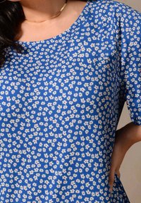 Modrá květinová blůza s kulatým výstřihem, krátkým rukávem a texturovanou látkou s malými bílými květy po celé ploše.