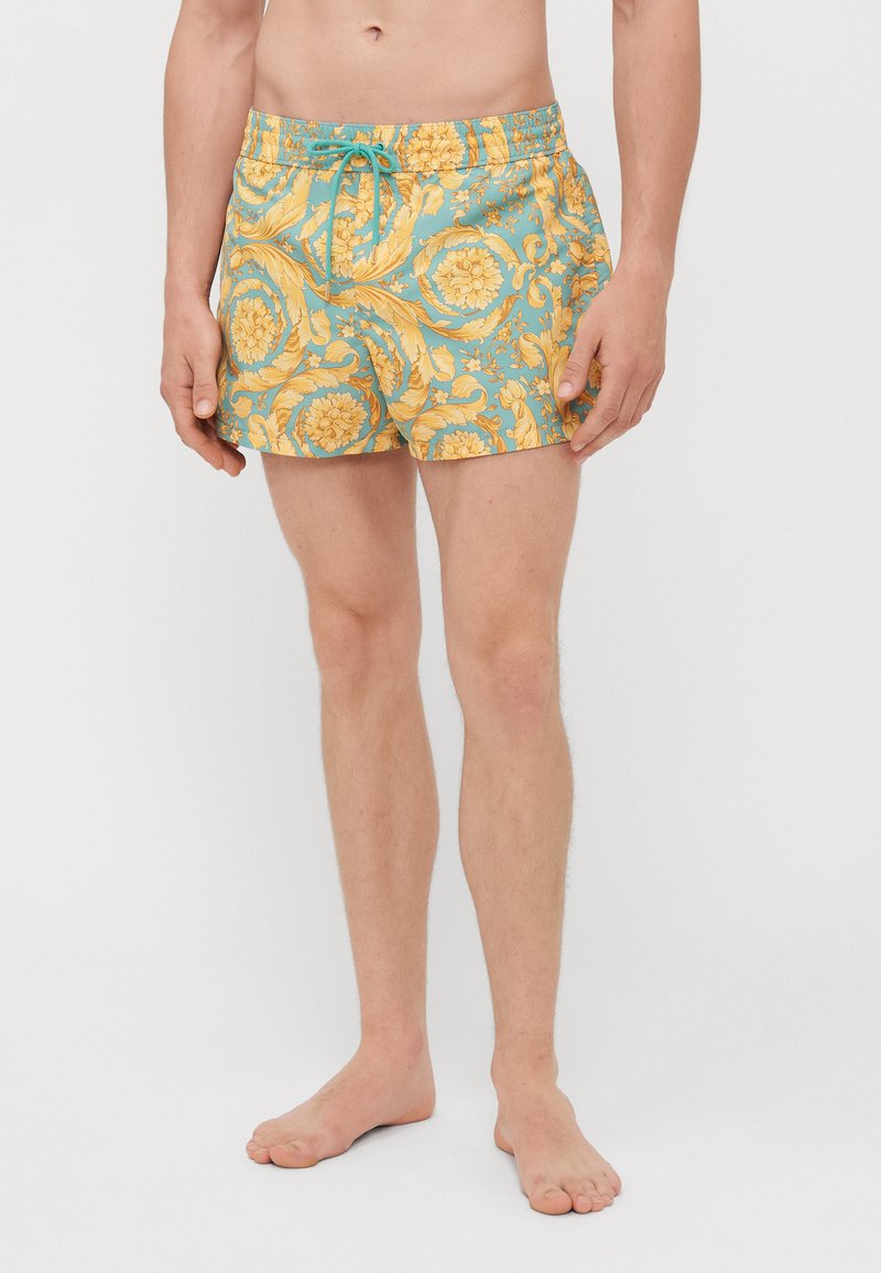Shorts de bain à motifs avec une base bleu clair ornée de fleurs jaunes et de motifs en spirale. Tissu léger avec une taille élastique et un cordon de serrage.