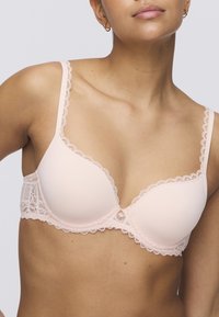 Light pink bra with lace trim, seamless cups, and decorative button detail at the center. Adjustable straps enhance fit and comfort.