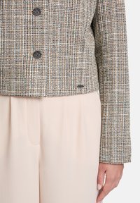Wool-blend cropped jacket in brown and cream check pattern, featuring two dark buttons and a smooth, fitted silhouette. Light beige trousers.