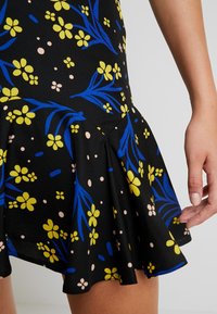 Gonna svasata in tessuto nero con un vivace motivo floreale con fiori gialli e blu. Tessuto liscio con orlo arricciato.