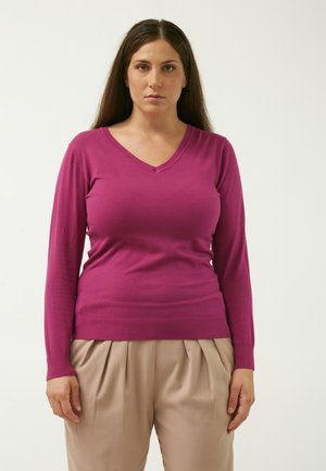 Maglione magenta a scollo a V con maniche lunghe, orlo e polsini a coste, realizzato in un tessuto morbido. Abbinato a pantaloni beige plissettati.
