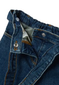 Donkerblauwe denim jeans hebben een tailleband met een elastische inzet, een metalen knoop en contrasterend oranje stiksels. De binnenvoering heeft een patronen.