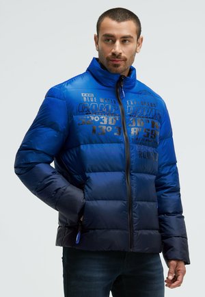 Blue puffer jacket with a high collar, featuring contrasting navy panels and printed text graphics. Zippered front and side pockets.