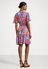 Vestido floral em azul claro, com padrões vibrantes em vermelho e laranja, mangas esvoaçantes, cintura ajustada e saia rodada. Sapatos de cunha castanhos.