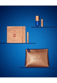 Augustinus Bader skincare set includes a metallic bronze pouch, blue serum, beige eye patches, and gold-accents with sleek packaging.