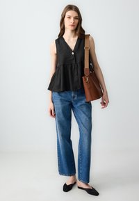 Top senza maniche in lino nero con vita a peplo, dettaglio con bottone singolo, abbinato a jeans blu a gamba dritta e una borsa marrone.