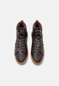 Barna magas szárú tornacipő, érdes bőrből, műszőrme béléssel, lekerekített orral, feketével fűzve és világosbarna gumitalppal.