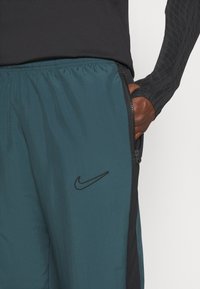 Tyrkysové sportovní šortky s černým bočním panelem a zipovou kapsou, se černým logem Nike. Vyrobeno z lehkého, texturovaného materiálu.