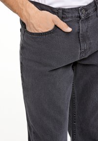 Pantalones de mezclilla gris oscuro con un diseño de pierna recta, que cuentan con bolsillos estándar y detalles de costura sutiles. La tela tiene una textura suave.