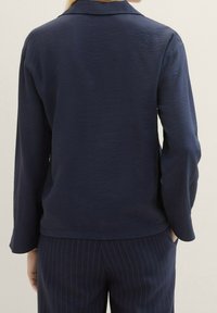 Chemise bleu marine à manches longues avec col, tissu texturé et ourlet droit, associée à un pantalon bleu marine à fines rayures.