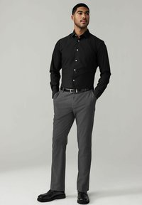 Schwarzes Langarmhemd mit weißen Knöpfen, kombiniert mit grauen Hosen und schwarzen Lederschuhen. Einfaches Design und taillierte Passform.