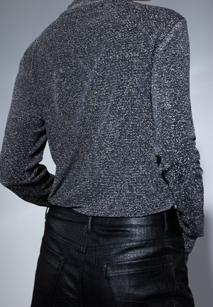 Długi rękaw, ciemny, nakrapiany top o fakturowanym wykończeniu, w połączeniu z dopasowanymi czarnymi spodniami z ekoskóry z wzorem w krokodyla.