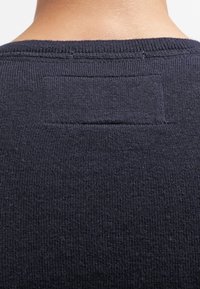 Granatowy sweter dzianinowy z fakturowanej tkaniny, okrągłym dekoltem i prostokątną metką z tyłu, podkreślający minimalistyczny design.