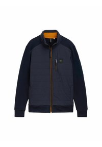 Jachetă matlasată de marină cu accente portocalii, guler înalt, închidere cu fermoar, buzunare laterale și panou texturat la mâneci. Include un patch cu logo pe piept.