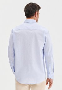 Jasnoniebieska koszula z długim rękawem, z zapięciem na guziki przy mankietach, prosta linia dołu, wykonana z miękkiego materiału, o gładkiej fakturze i subtelnym połysku.