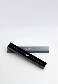 Guldring med et bladdesign på en delikat kæde, præsenteret i en sort boks med blank finish og logo på låget.