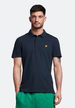 Polo shirt marine en coton avec un col classique, trois boutons et un petit emblème d'aigle jaune sur la poitrine gauche. Manches courtes.