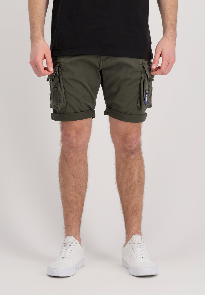 Olive green cargo shorts with side pockets, cuffed hems, and a smooth cotton texture. Worn with white sneakers and a black t-shirt.